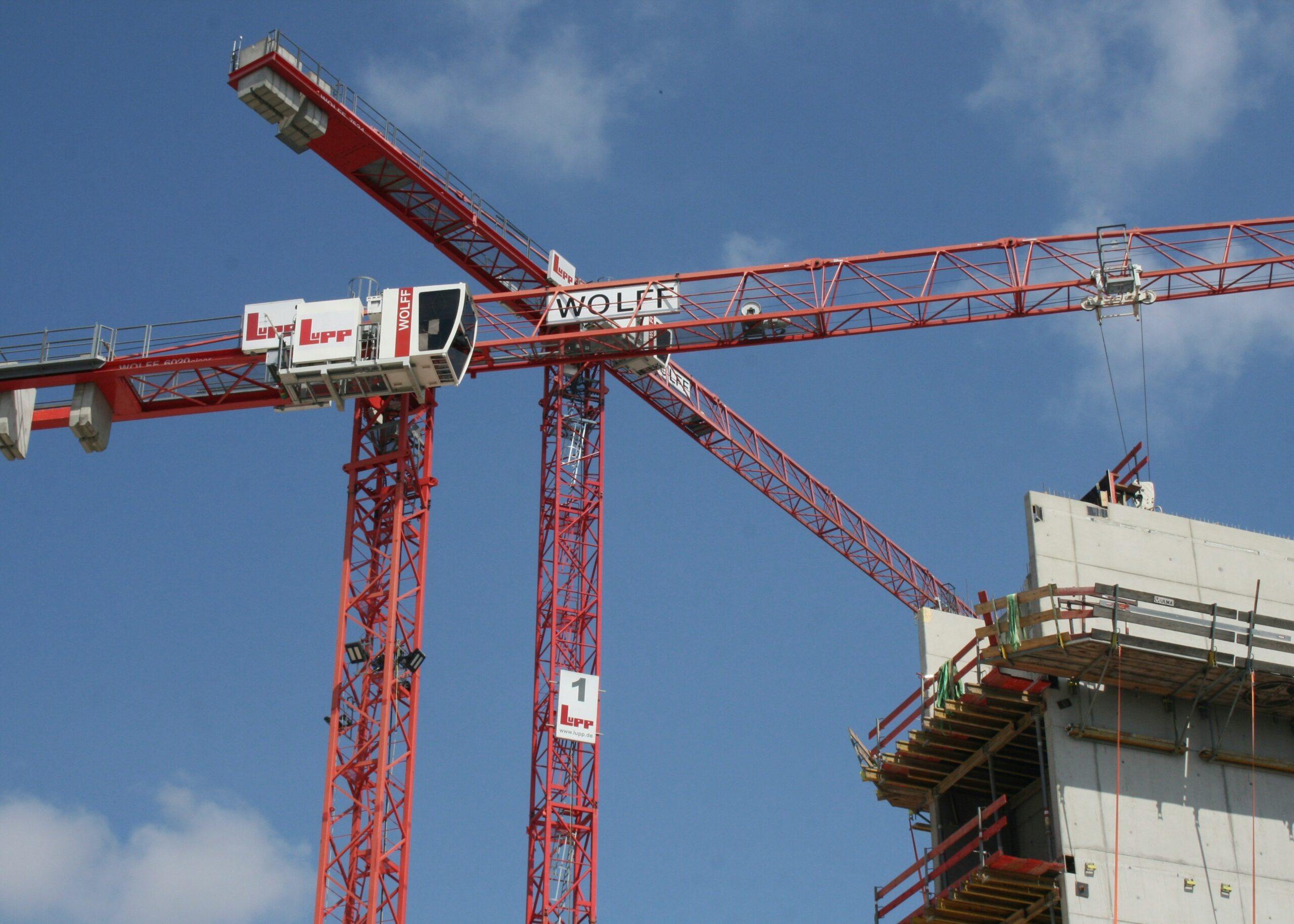 Two red tower cranes beside a concrete building under construction