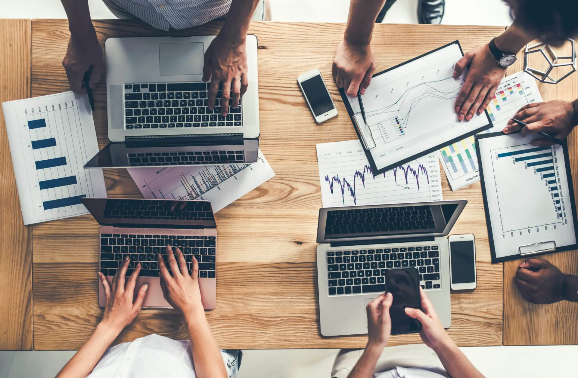 A group of people working around a table with laptops and chart printouts.